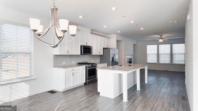 kitchen with ceiling fan with notable chandelier, stainless steel appliances, a kitchen island with sink, and white cabinets