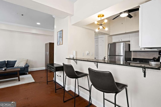 kitchen with stainless steel fridge, pendant lighting, white cabinetry, and a breakfast bar area