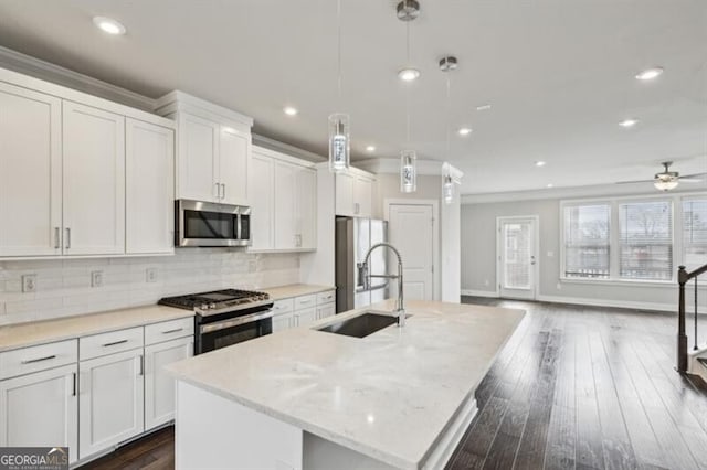 kitchen featuring appliances with stainless steel finishes, pendant lighting, white cabinetry, sink, and a center island with sink