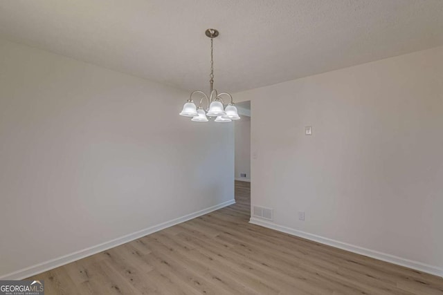 unfurnished room with a notable chandelier and light hardwood / wood-style floors