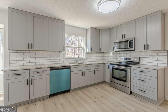 kitchen featuring light stone counters, a textured ceiling, stainless steel appliances, gray cabinets, and sink