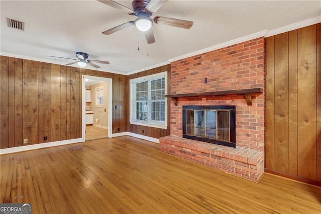 unfurnished living room featuring a fireplace, ceiling fan, hardwood / wood-style flooring, wood walls, and crown molding