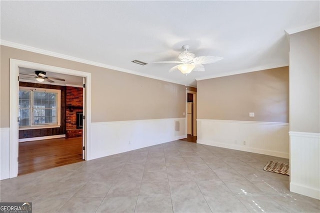 tiled empty room with a brick fireplace, ceiling fan, and crown molding