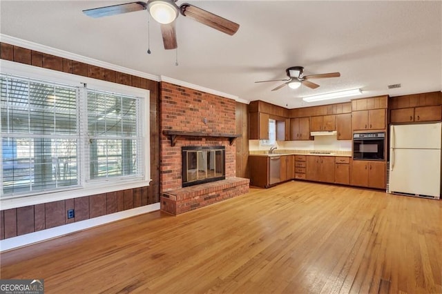 kitchen featuring black appliances, light hardwood / wood-style floors, ornamental molding, a brick fireplace, and sink