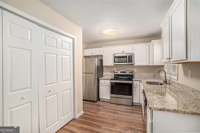 kitchen featuring stainless steel appliances, white cabinets, sink, and light stone counters