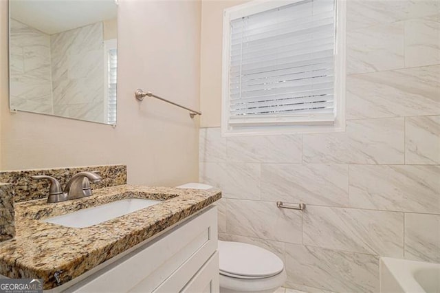 bathroom featuring tile walls, a bathtub, vanity, and toilet