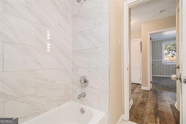 bathroom with a textured ceiling, wood-type flooring, and tiled shower / bath