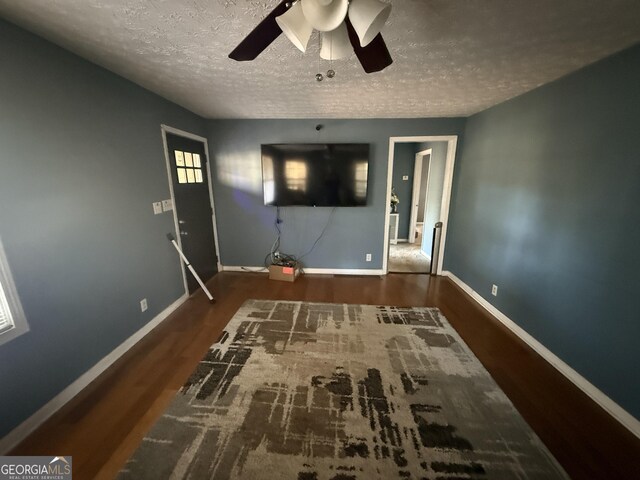 unfurnished living room with a textured ceiling, ceiling fan, and dark wood-type flooring