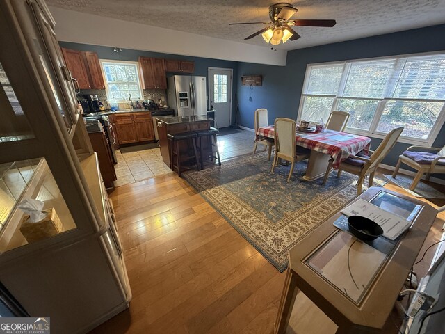 dining room with a textured ceiling, ceiling fan, a healthy amount of sunlight, and light hardwood / wood-style floors