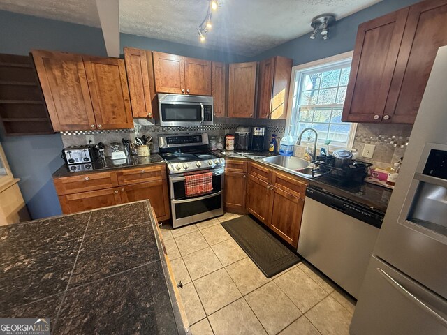 kitchen with appliances with stainless steel finishes, light tile patterned floors, decorative backsplash, a textured ceiling, and sink