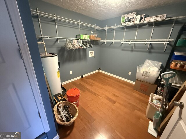 clothes washing area featuring a textured ceiling, water heater, and wood-type flooring