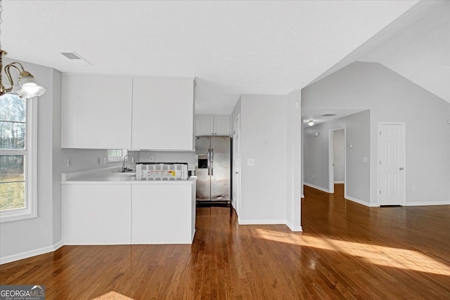 kitchen with a notable chandelier, kitchen peninsula, stainless steel refrigerator with ice dispenser, sink, and white cabinets