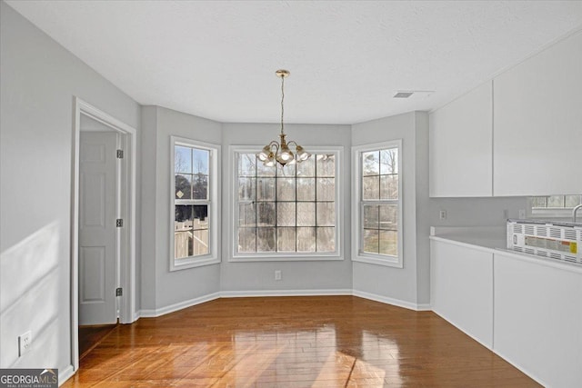 unfurnished dining area featuring plenty of natural light, hardwood / wood-style floors, a textured ceiling, and a notable chandelier