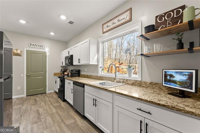 kitchen with visible vents, white cabinetry, a sink, light stone countertops, and black appliances