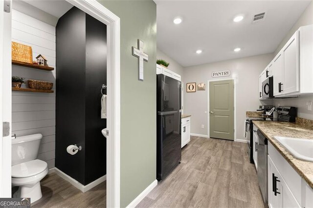 kitchen with black appliances, white cabinets, light stone counters, and sink