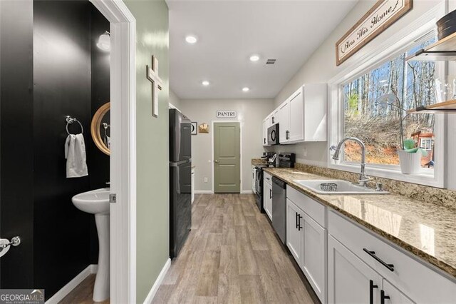 kitchen with stainless steel appliances, sink, white cabinetry, light wood-type flooring, and light stone countertops