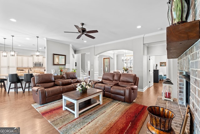 living room featuring ceiling fan with notable chandelier, wood-type flooring, a fireplace, and crown molding