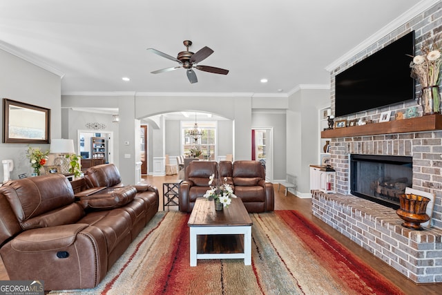 living room featuring a fireplace, crown molding, ceiling fan with notable chandelier, and hardwood / wood-style flooring