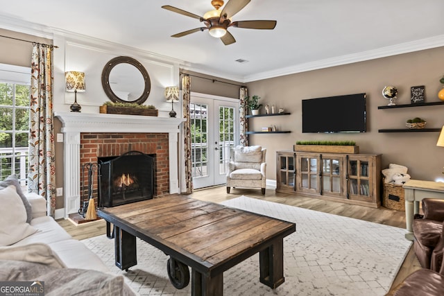 living room with a fireplace, french doors, ceiling fan, light hardwood / wood-style floors, and crown molding