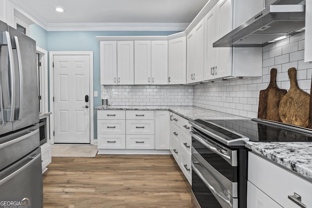 kitchen with stainless steel appliances, light stone counters, white cabinetry, wall chimney range hood, and backsplash