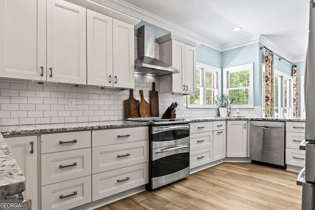 kitchen featuring appliances with stainless steel finishes, light stone countertops, decorative backsplash, wall chimney exhaust hood, and white cabinets