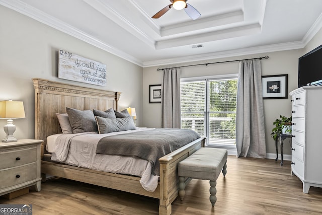 bedroom with ceiling fan, crown molding, hardwood / wood-style flooring, and a tray ceiling