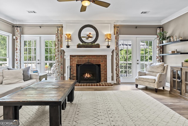 living room featuring french doors, crown molding, a fireplace, ceiling fan, and wood-type flooring