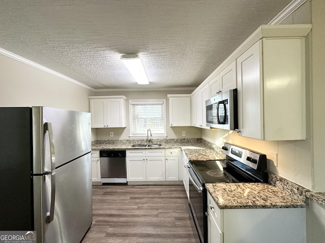 kitchen with appliances with stainless steel finishes, ornamental molding, a textured ceiling, white cabinets, and sink