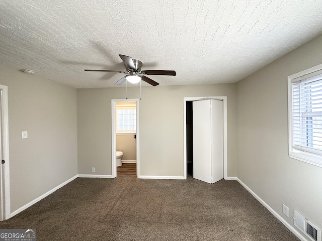 unfurnished bedroom featuring a textured ceiling, connected bathroom, ceiling fan, dark carpet, and a closet