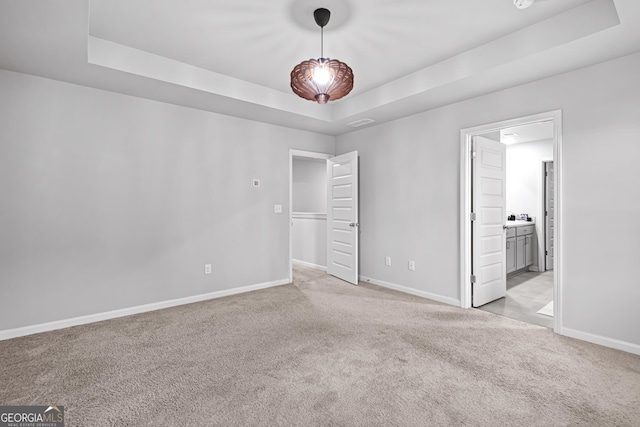 unfurnished bedroom featuring a raised ceiling, light colored carpet, and connected bathroom