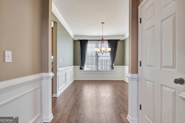 unfurnished dining area with dark wood-style floors, a notable chandelier, wainscoting, and crown molding