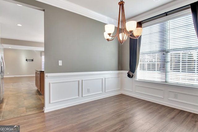 unfurnished dining area with crown molding, wainscoting, wood finished floors, a notable chandelier, and a decorative wall