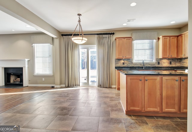 kitchen with baseboards, a fireplace with raised hearth, a sink, decorative backsplash, and open floor plan