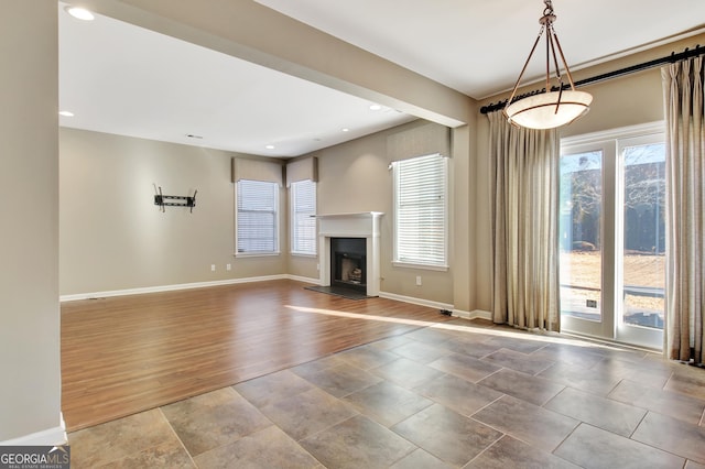 unfurnished living room with wood finished floors, recessed lighting, a fireplace with raised hearth, and baseboards