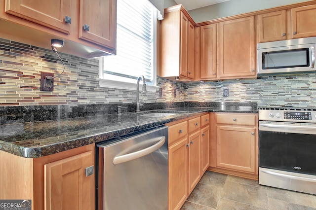 kitchen featuring a sink, dark stone countertops, stone finish flooring, appliances with stainless steel finishes, and decorative backsplash