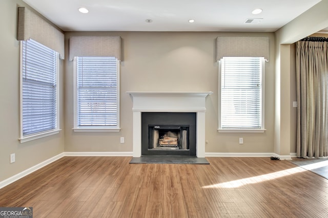 unfurnished living room with baseboards, wood finished floors, visible vents, and a fireplace with raised hearth