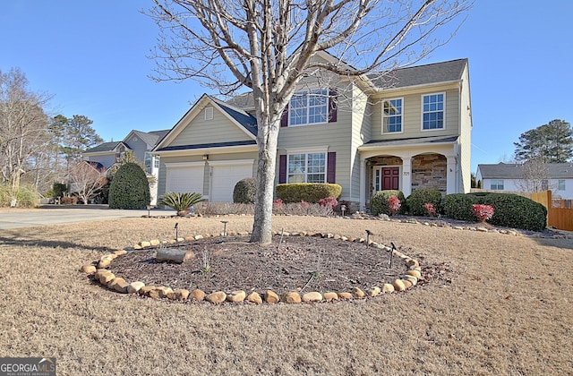 traditional home featuring stone siding, an attached garage, driveway, and fence