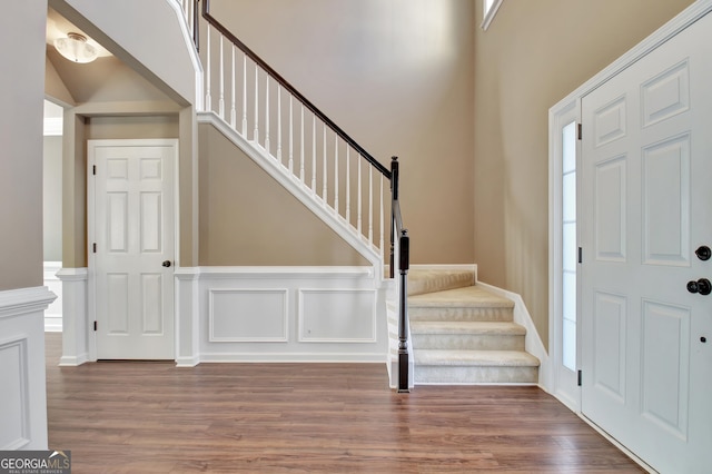 entrance foyer featuring stairway, a decorative wall, a wainscoted wall, and wood finished floors