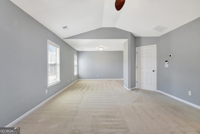 spare room with light colored carpet, lofted ceiling, baseboards, and visible vents