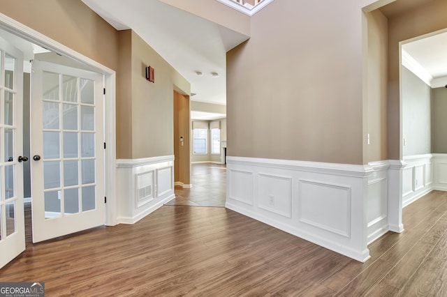 foyer featuring french doors, wood finished floors, wainscoting, and a decorative wall