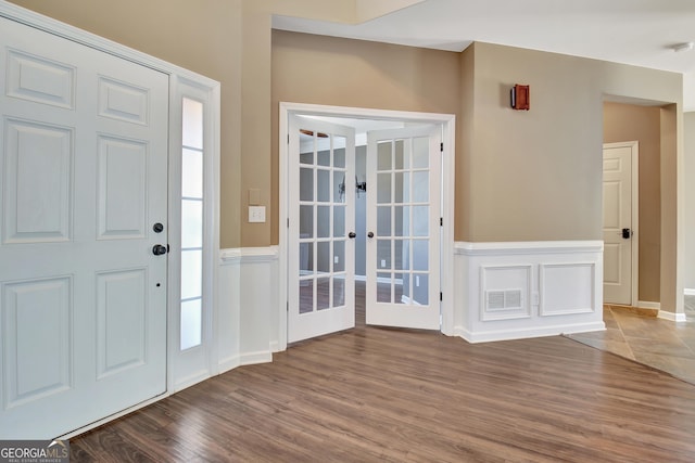 foyer featuring wood finished floors, visible vents, french doors, and wainscoting