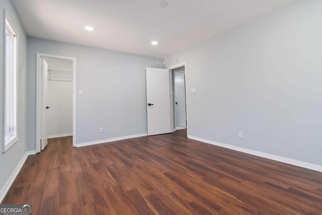 unfurnished bedroom featuring a walk in closet, a closet, and dark wood-type flooring