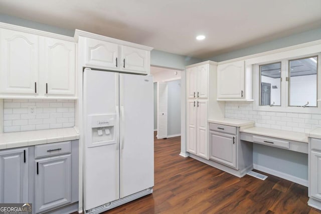 kitchen featuring built in desk, white cabinets, tasteful backsplash, and white fridge with ice dispenser