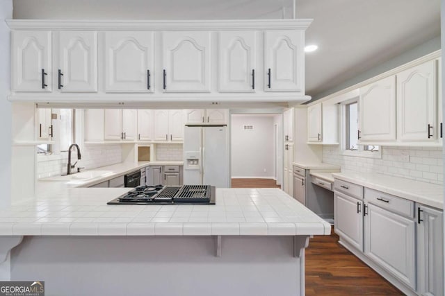 kitchen with black appliances, kitchen peninsula, tile countertops, white cabinets, and sink