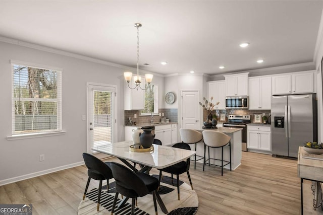 dining area featuring ornamental molding, light wood-type flooring, a notable chandelier, and sink