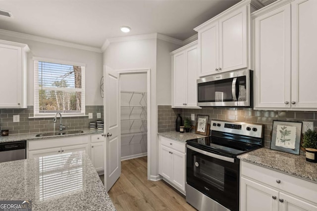 kitchen featuring sink, white cabinetry, light stone counters, light hardwood / wood-style flooring, and appliances with stainless steel finishes