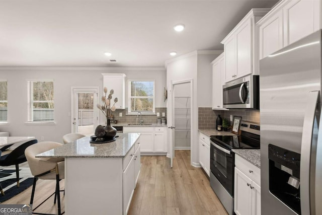 kitchen with stainless steel appliances, a center island, a breakfast bar, light stone counters, and white cabinets