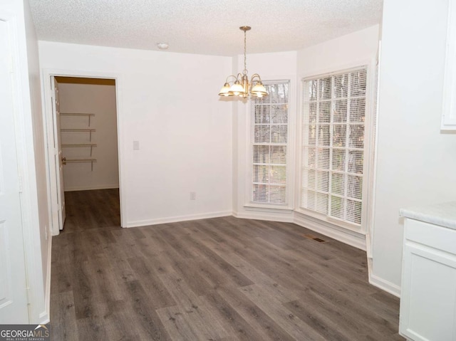 unfurnished dining area with a textured ceiling, a notable chandelier, and dark hardwood / wood-style floors