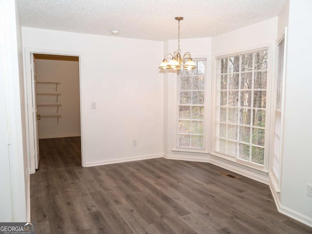 unfurnished dining area featuring dark hardwood / wood-style flooring, a textured ceiling, and a notable chandelier