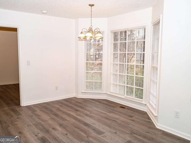 unfurnished dining area with a textured ceiling, a chandelier, and dark hardwood / wood-style floors